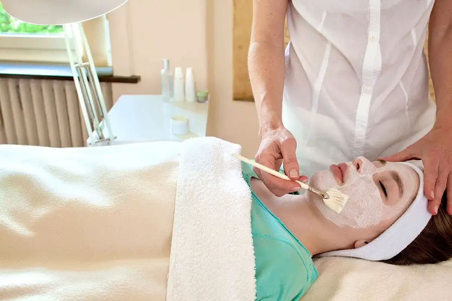 cosmetician applying a mask on a woman's face as she is laying down