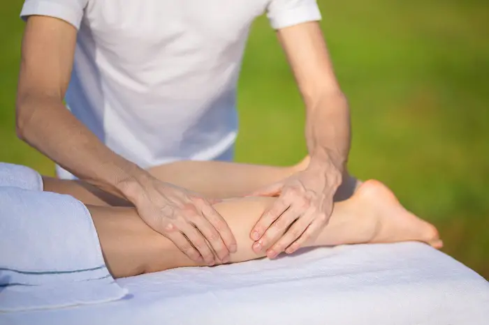 Massage of gastrocnemius muscle to young girl outside.
