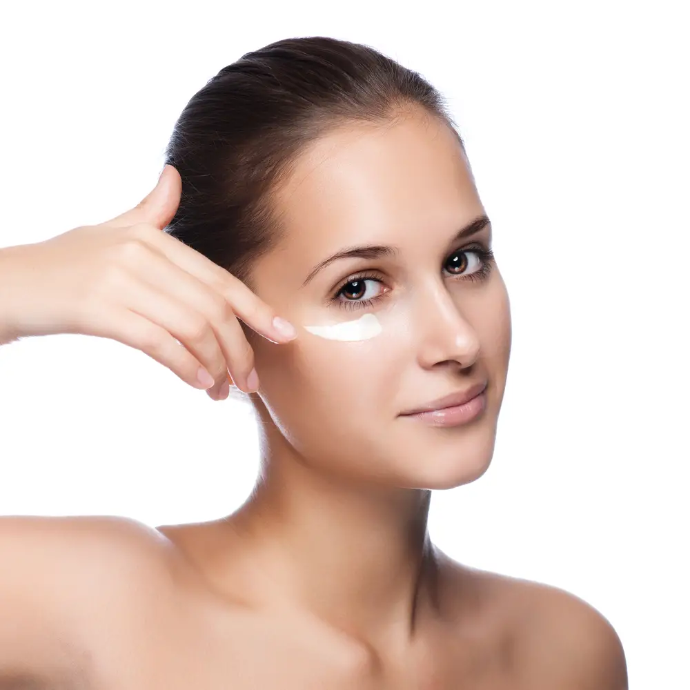 Young woman applying face cream under her eyes